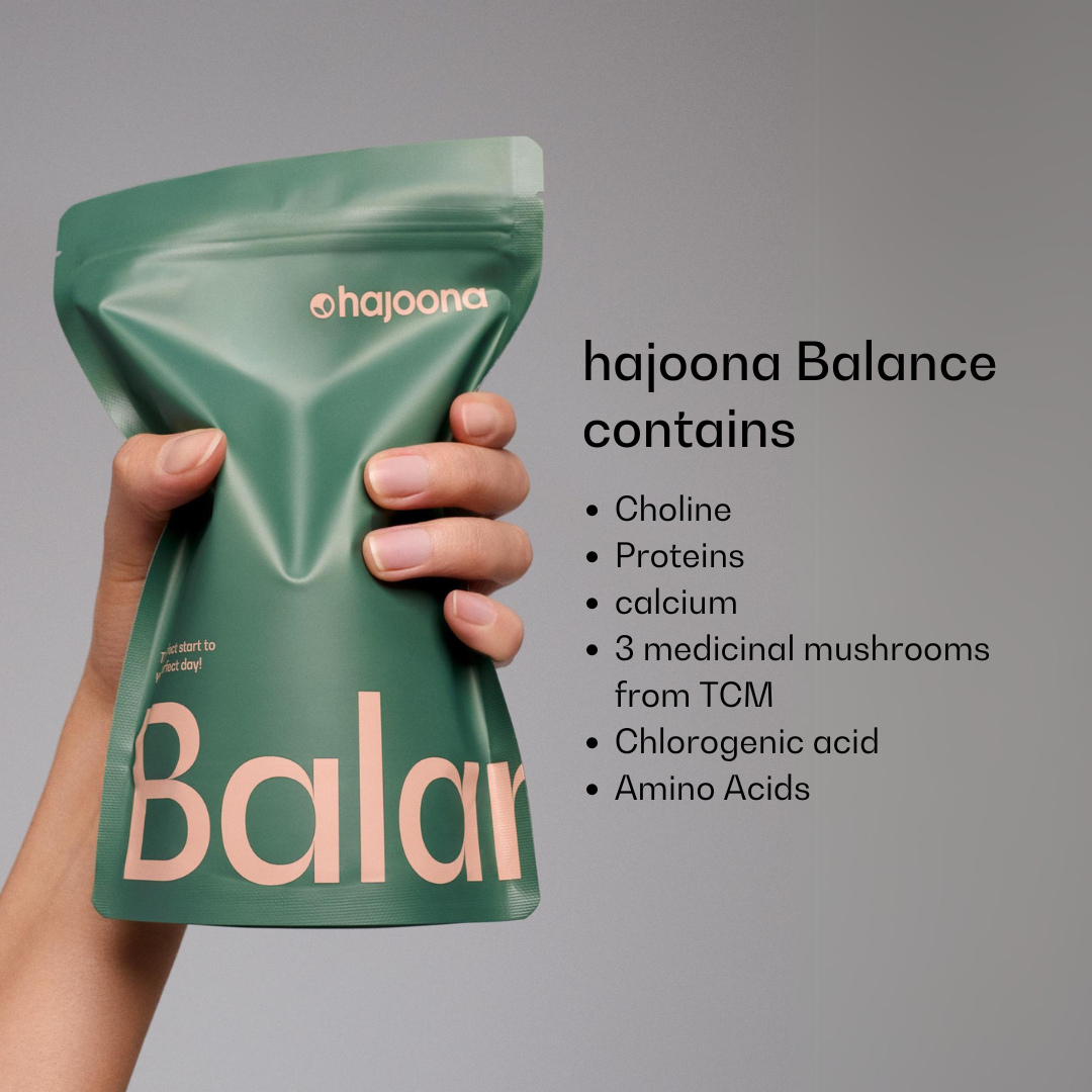 In one hand is a green Hajoona Balance refill bag with a pink label. The ingredients are listed to the right: Choline, proteins, calcium, medicinal mushrooms from Traditional Chinese Medicine (TCM), chlorogenic acid and amino acids.