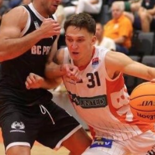 Zwei Basketballspieler im Duell. Der Profi-Basketballer Lukas Reichle trägt ein weißesn Trikot mit orangen Streifen, er dribbelt einen orangefarbenen Ball. Der andere Spieler im schwarzen Trikot versuch ihn zu stoppen. Der Boden ist orange, im Hintergrund sitzen Zuschauer.