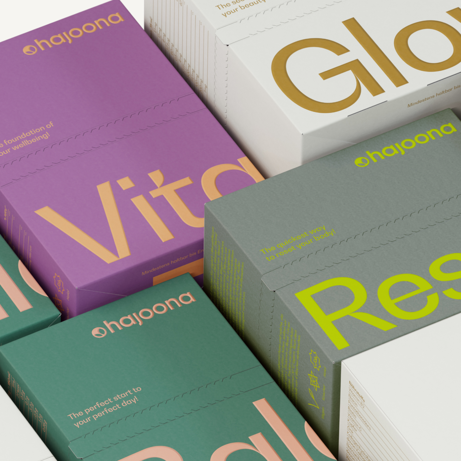 Mehrere bunte Produktverpackungen der Marke hajoona liegen dicht aneinandergereiht. Sichtbar sind die Produktnamen Glow, Vita, Balance und Reset in großen, farblich abgesetzten Buchstaben. Die Verpackungen sind modern gestaltet und in verschiedenen Farben gehalten, wie Lila, Weiß, Grün und Grau.