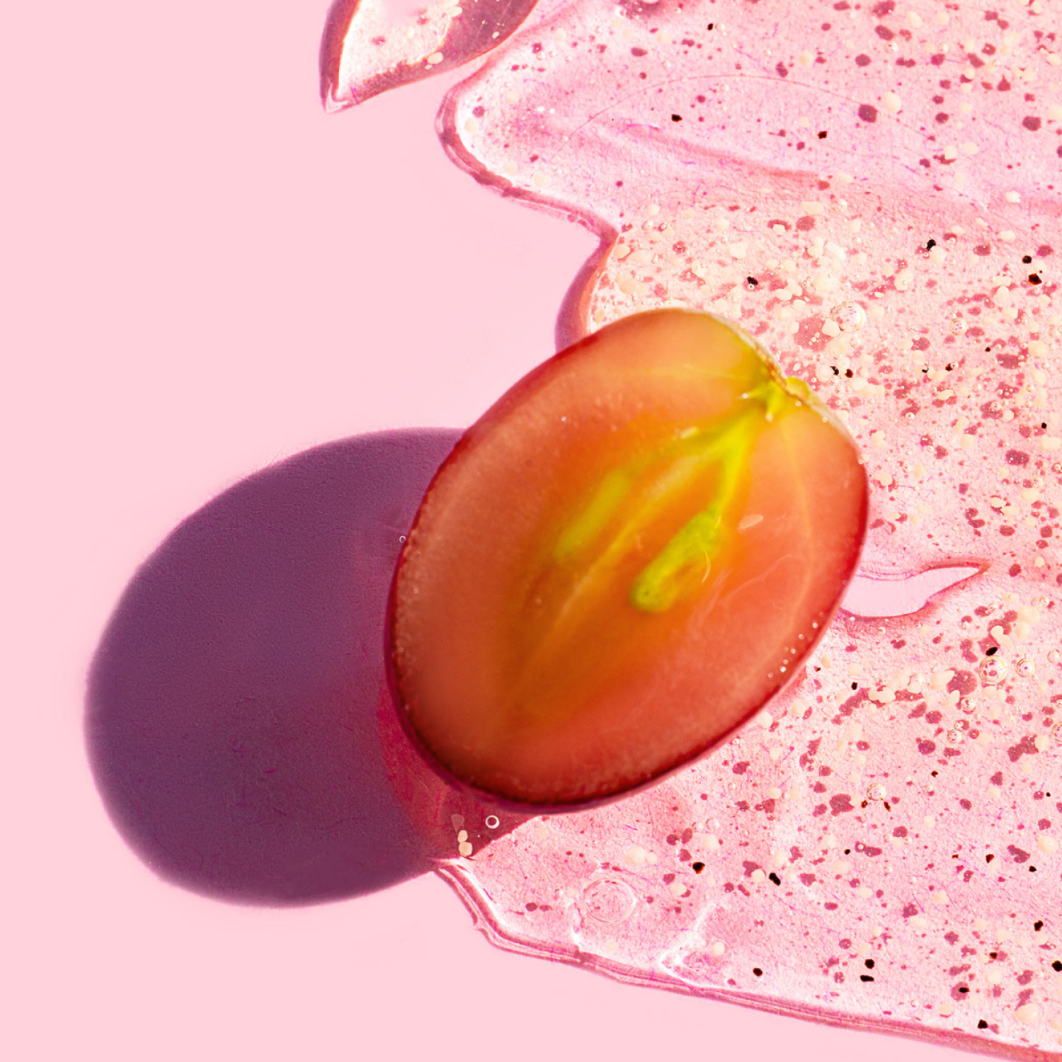 Nahaufnahme einer halbierten roten Weintraube auf rosafarbenem Hintergrund mit glänzendem, transparentem Gel. Symbol für natürliche Polyphenole, Frische und moderne Produktästhetik.
