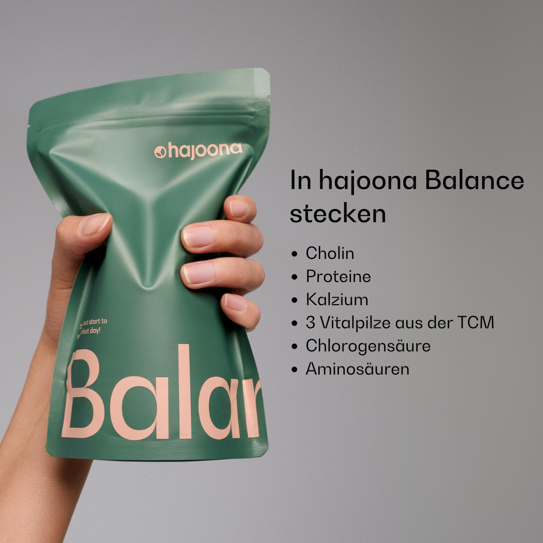 Eine Hand hält einen grünen hajoona Balance Nachfüllbeutel mit rosafarbener Aufschrift. Rechts daneben sind die Inhaltsstoffe aufgeführt: Cholin, Proteine, Calcium, medizinische Pilze aus der TCM, Chlorogensäure und Aminosäuren.