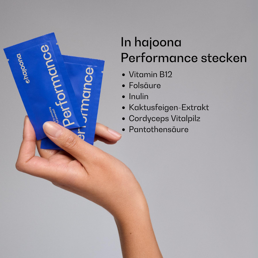 Hand hält zwei blaue hajoona Performance Sachets. Rechts im Bild sind die enthaltenen Wirkstoffe aufgelistet: Vitamin B12, Folsäure, Inulin, Kaktusfeigenextrakt, Cordyceps-Pilz und Pantothensäure.