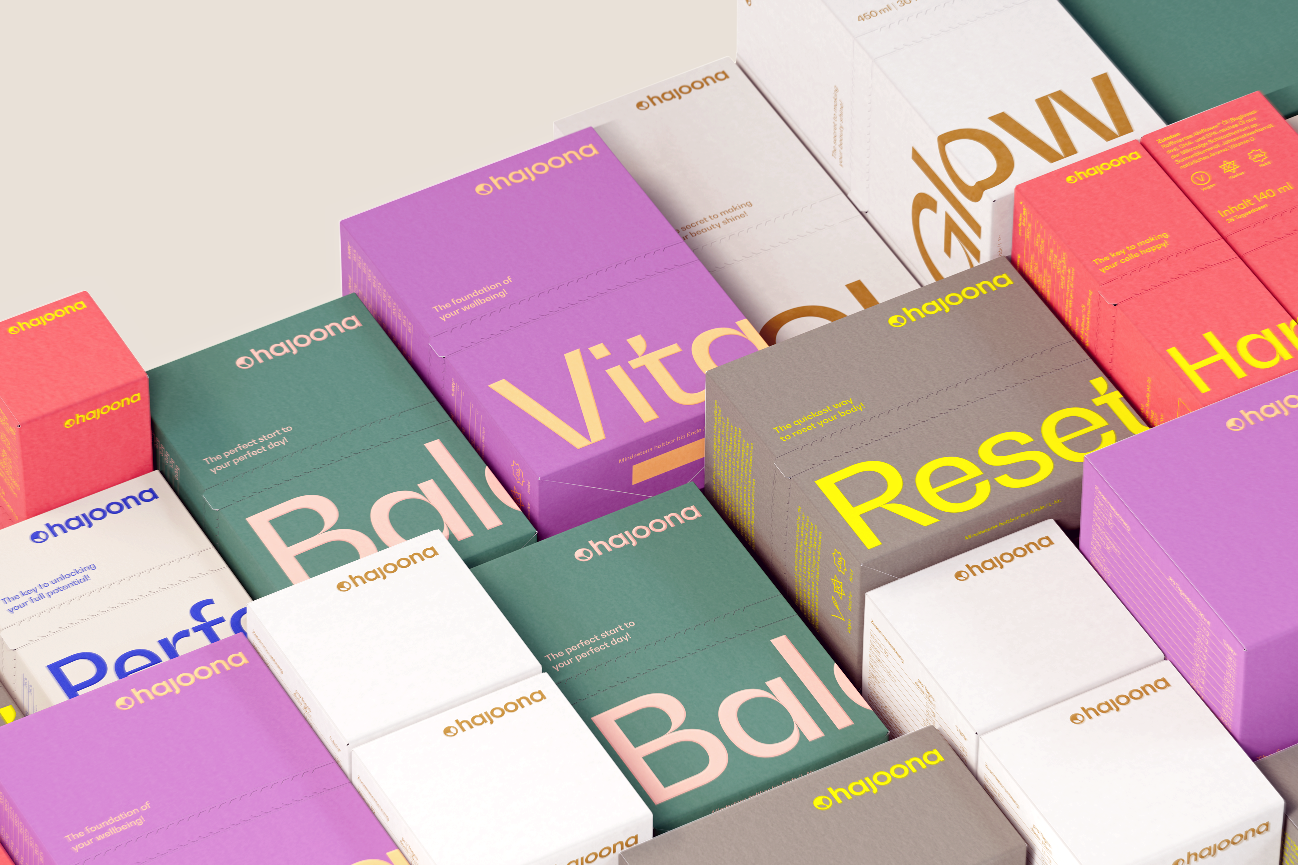 Mehrere bunte Produktverpackungen der Marke hajoona liegen dicht aneinandergereiht. Sichtbar sind die Produktnamen Glow, Vita, Balance und Reset in großen, farblich abgesetzten Buchstaben. Die Verpackungen sind modern gestaltet und in verschiedenen Farben gehalten, wie Lila, Weiß, Grün und Grau.
